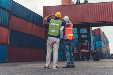 Industrial worker works with co-worker at overseas shipping container yard . Logistics supply chain management and international goods export concept .の写真素材