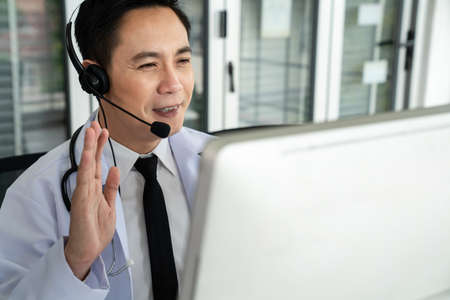 Doctor wearing headset talking actively on video call in a clinic or hospital . Concept of telehealth and telemedicine service .の写真素材