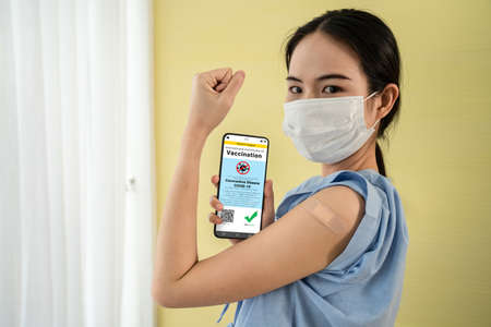 Young Asian woman shows vaccine passport on mobile phone to validate travel permission by the digital documentの写真素材