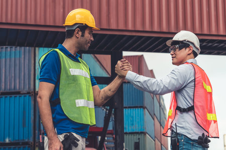 Industrial worker works with co-worker at overseas shipping container yard . Logistics supply chain...