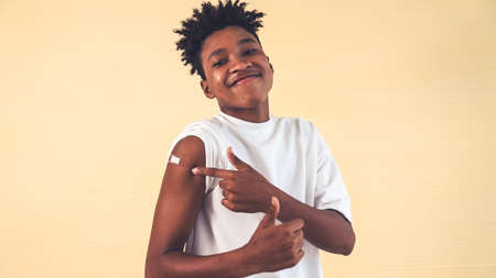African American teenager showing COVID-19 vaccine bandage merrily in concept of coronavirus vaccination program to vaccinate citizen .の写真素材