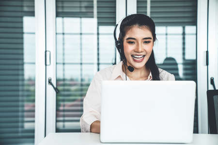 Businesswoman wearing headset working actively in office . Call center, telemarketing, customer support agent provide service on telephone video conference call.の写真素材