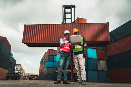 Industrial worker works with co-worker at overseas shipping container yard . Logistics supply chain management and international goods export concept .の写真素材