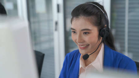 Businesswoman wearing headset working actively in office . Call center, telemarketing, customer support agent provide service on telephone video conference call.の写真素材