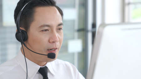 Businessman wearing headset working actively in office . Call center, telemarketing, customer support agent provide service on telephone video conference call.の写真素材