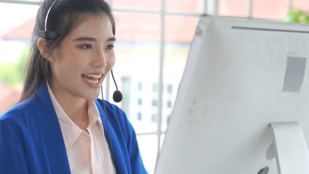 Businesswoman wearing headset working actively in office . Call center, telemarketing, customer support agent provide service on telephone video conference call.の写真素材