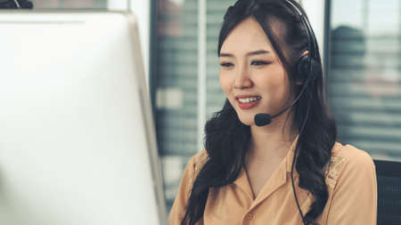Businesswoman wearing headset working actively in office . Call center, telemarketing, customer support agent provide service on telephone video conference call.の写真素材