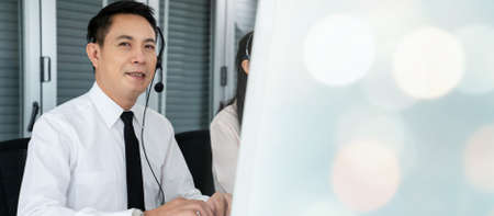 Businessman wearing headset working actively in office . Call center, telemarketing, customer support agent provide service on telephone video conference call.の写真素材