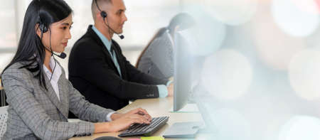Business people wearing headset working in office to support remote customer or colleague. Call center, telemarketing, customer support agent provide service in broaden view .の写真素材