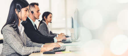 Business people wearing headset working in office to support remote customer or colleague. Call center, telemarketing, customer support agent provide service in broaden view .の写真素材