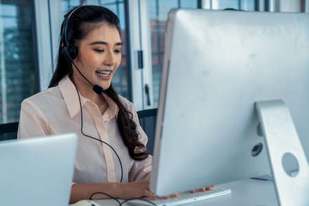 Businesswoman wearing headset working actively in office . Call center, telemarketing, customer support agent provide service on telephone video conference call.の写真素材