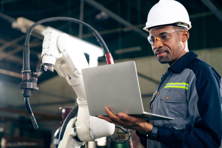 African American factory worker working with adept robotic arm in a workshop . Industry robot...