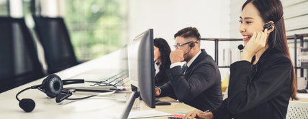 Business people wearing headset working in office to support remote customer or colleague. Call center, telemarketing, customer support agent provide service in broaden view .の写真素材