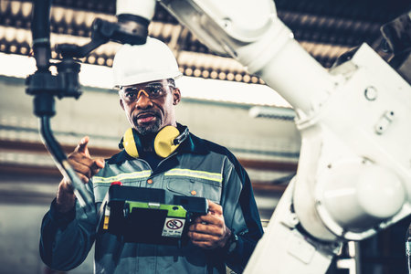 African American factory worker working with adept robotic arm in a workshop . Industry robot...