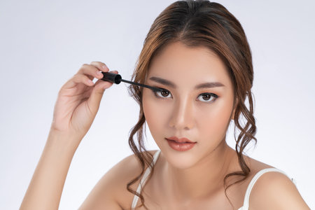 Closeup gorgeous young woman putting black mascara on her long eyelashes with brush. Beauty cosmetic...