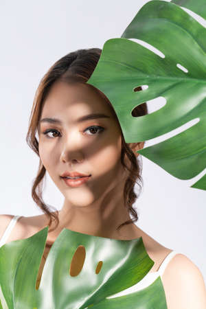 Closeup portrait of young gorgeous woman with healthy fair skin holding big green leaf near her face. Skin care beauty care concept.の写真素材