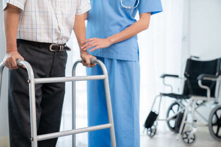 Physiotherapist assists her contented senior patient on folding walker. Recuperation for elderly, seniors care, nursing home.の写真素材