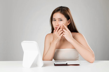 Portrait of young ardent asian woman looking in the mirror worry about pimple on her face. Beauty...