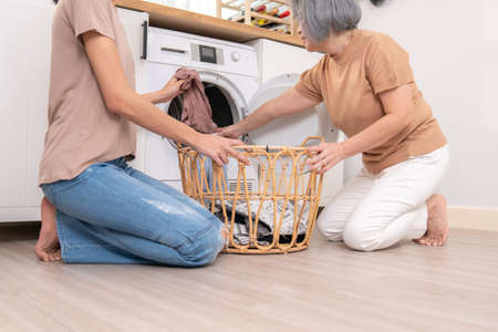 Daughter and mother working together to complete their household chores near the washing machine in a happy and contented manner. Mother and daughter doing the usual tasks in the house.の写真素材