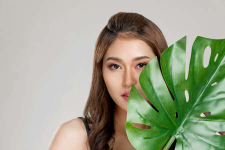 Closeup portrait of young ardent woman with healthy fair skin holding big green leaf near her face. Skin care beauty care concept.の写真素材