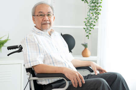 Portrait of an elderly man in a wheelchair alone with himself at home but contented with his lot in life. Convalescent facility for the crippled elderly in a nursing home.の写真素材