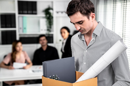 Depressed and disappointed employee packing his belongings after being fired for not being...