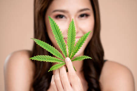 Closeup portrait of young ardent girl with healthy fresh skin holding green hemp leaf. Combination of beauty and cannabis concept.の写真素材