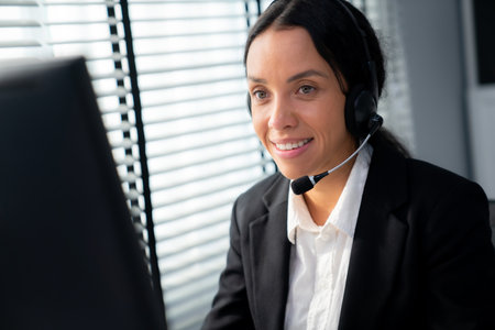 Competent female operator working on computer and talking with clients. Concept relevant to both call centers and customer service offices.の写真素材