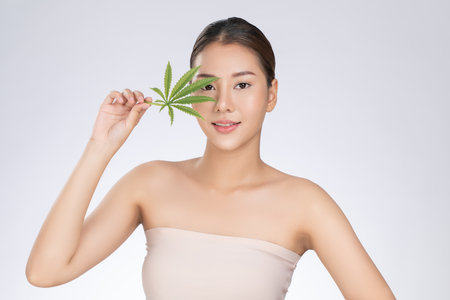 Portrait of young gorgeous girl with healthy fresh skin holding green hemp leaf. Combination of beauty and cannabis concept.の写真素材