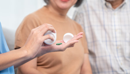 Contented senior woman sit along side with her husband, taking medicines while her caregiver advising her medication. Medication for seniors, nursing house, healthcare at home.の写真素材