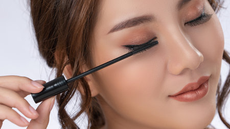 Closeup gorgeous young woman putting black mascara on her long eyelashes with brush. Beauty cosmetic concept. Female model with perfect skin.の写真素材