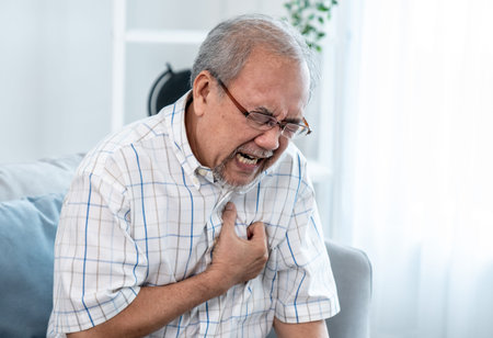 An agonizing senior man suffering from chest pain or heart attack alone in his living room. Serious...