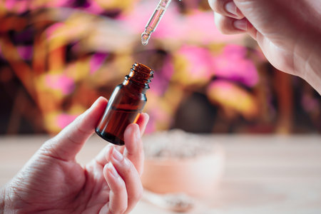 Hands holding a bottle of CBD oil and its dropper lid, with hemp leaf in the background. Legalized...