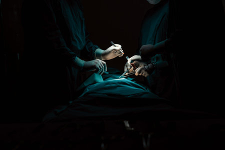 Surgical team performing surgery to patient in sterile operating room. In a surgery room lit by a lamp, a professional and confident surgical team provides medical care to an unconscious patient.の写真素材