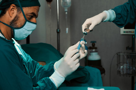 Surgeon fill syringe from medical vial for surgical procedure at sterile operation room with assistance nurse. Doctor and medical staff in full protective wear for surgery prepare anesthesia injectionの写真素材