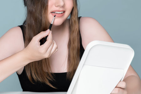 Beautiful young girl with perfect skin and makeup apply pink lipstick on herself. charming young...