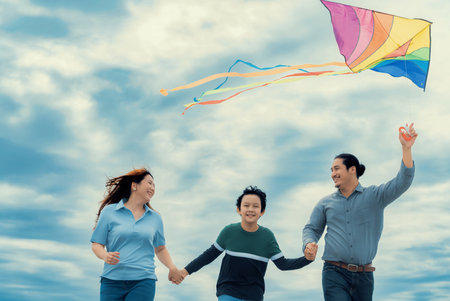 Progressive happy family vacation and carefree day concept. Young parents mother father and son run along and flying kite together road with enjoy natural scenic on scenery and clear sky background.の写真素材