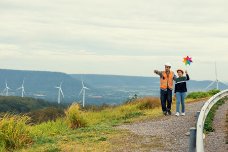 Engineer with his son holding windmill toy on a wind farm atop a hill or mountain. Progressive ideal...