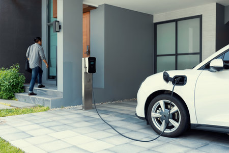 Progressive asian man and electric car with home charging station. Concept of the use of electric vehicles in a progressive lifestyle contributes to a clean and healthy environment.の写真素材