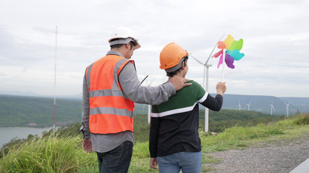 Engineer with his son on a wind farm atop a hill or mountain in the rural. Progressive ideal for the...