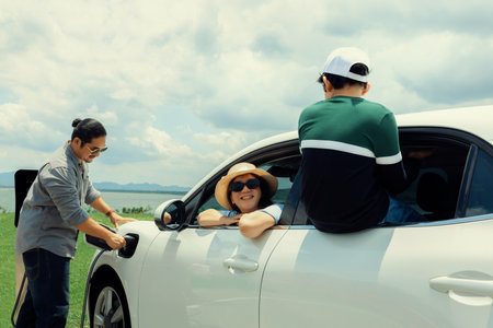 Concept of progressive happy family enjoying their time at green field and lake with electric vehicle. Electric vehicle driven by clean renewable from eco-friendly power sauce.の写真素材