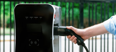Closeup progressive man holding EV charger plug from public charging station for electric vehicle...