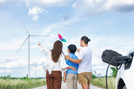Concept of progressive happy family holding windmill toy and relax at wind farm with electric...