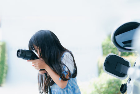 A playful girl holding and pointing an EV plug, a home charging station providing a sustainable power source for electric vehicles. Concept of progressive new generation with ecological awareness.の写真素材