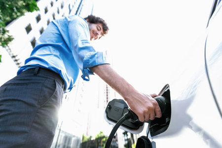 Fish eye view focus on hand insert EV charger plug into electric car with blur background of...
