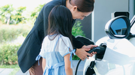 Progressive lifestyle of mother and daughter who have just returned from school in an electric vehicle that is being charged at home. Electric vehicle powered by sustainable clean energy.の写真素材