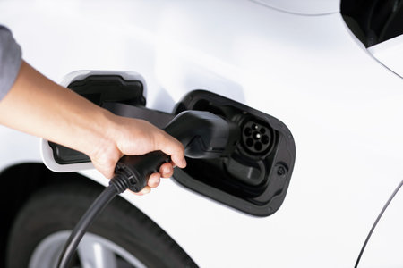 Closeup focus hand insert EV charger plug to electric vehicle from charging station. Progressive...