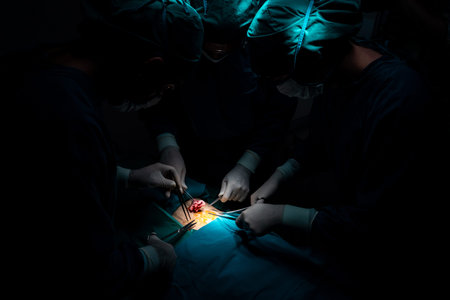 Surgical team performing surgery to patient in sterile operating room. In a surgery room lit by a...