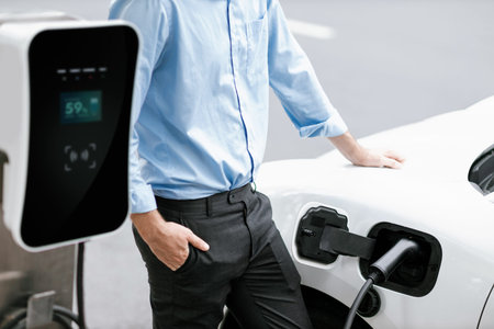 Closeup progressive suit-clad businessman with his electric vehicle recharge his car on public...