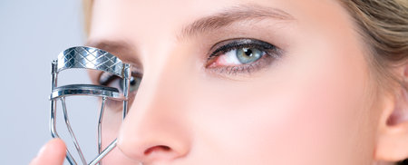 Closeup alluring facial makeup, beautiful woman with perfect smooth cosmetic clean skin correct eyelash curler with metal mechanic beauty accessory in isolated background.の写真素材